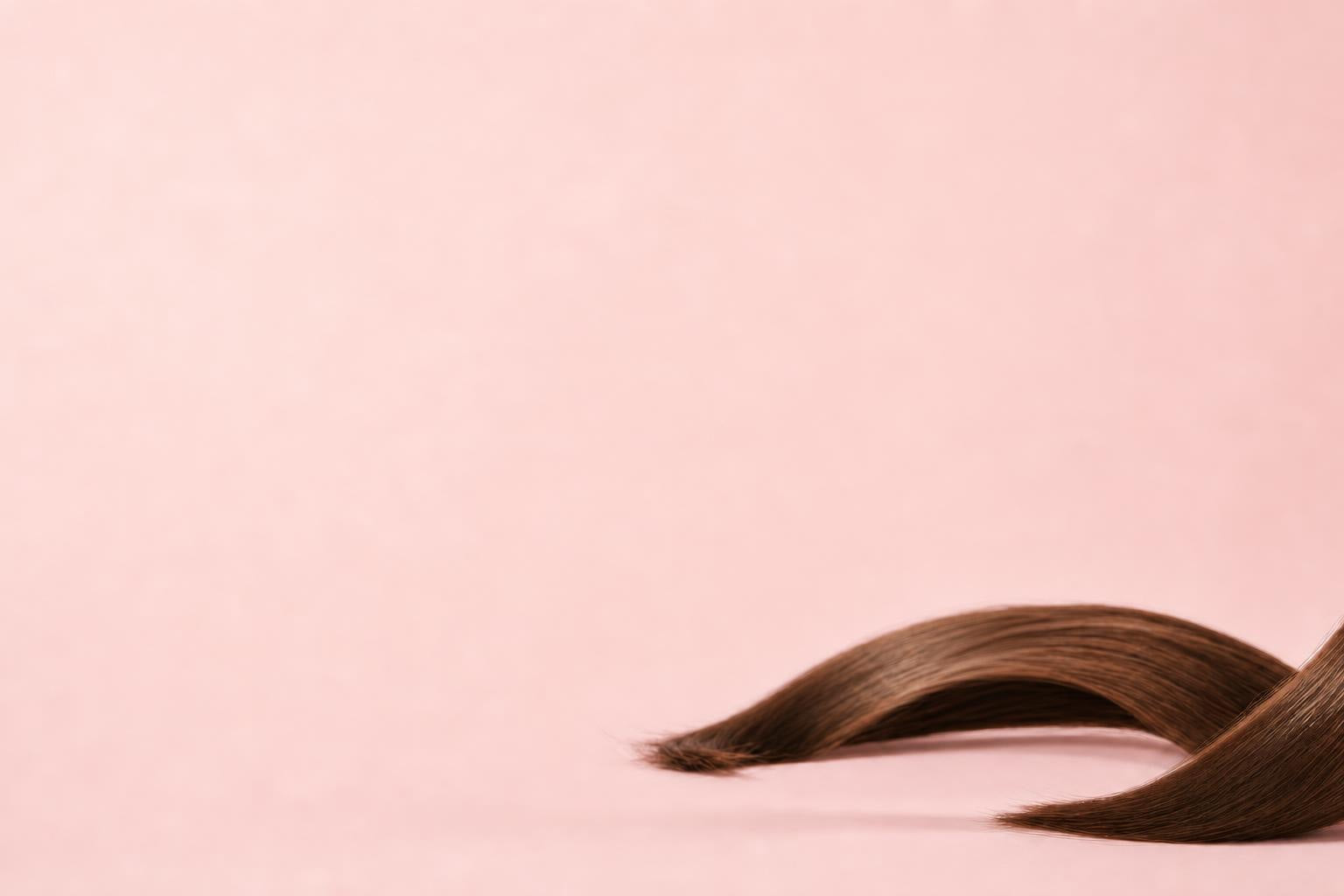 Silky strand of brown hair on a blush background